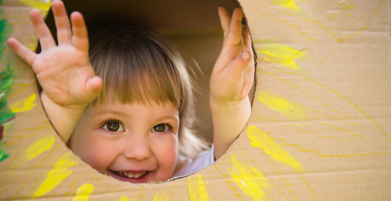 Little child looking through window of children's house made of big box